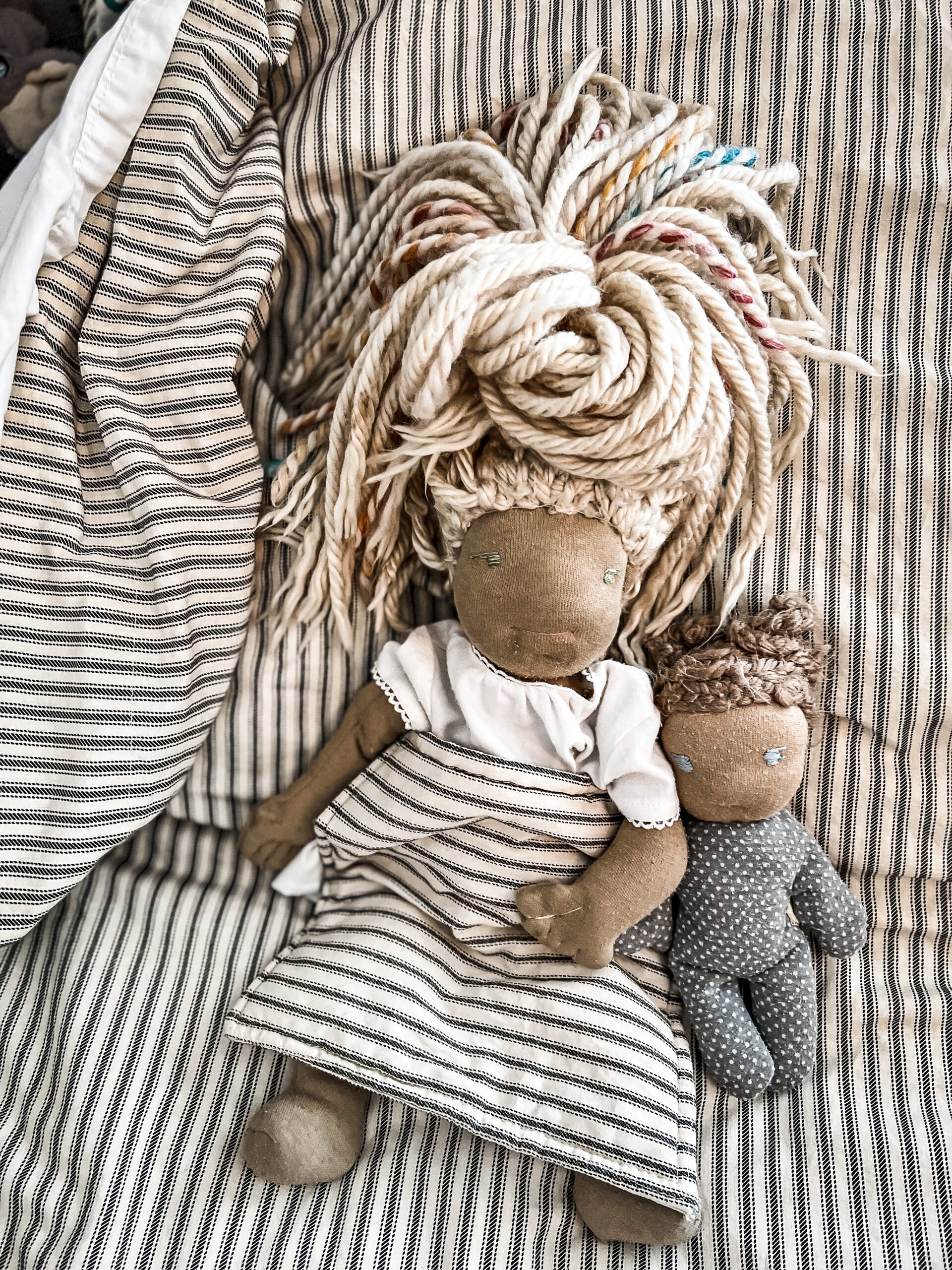 two dolls laying on stripped sheets